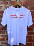 White t-shirt with red text 'good times pasta bar' on a wooden hanger against a brick wall.